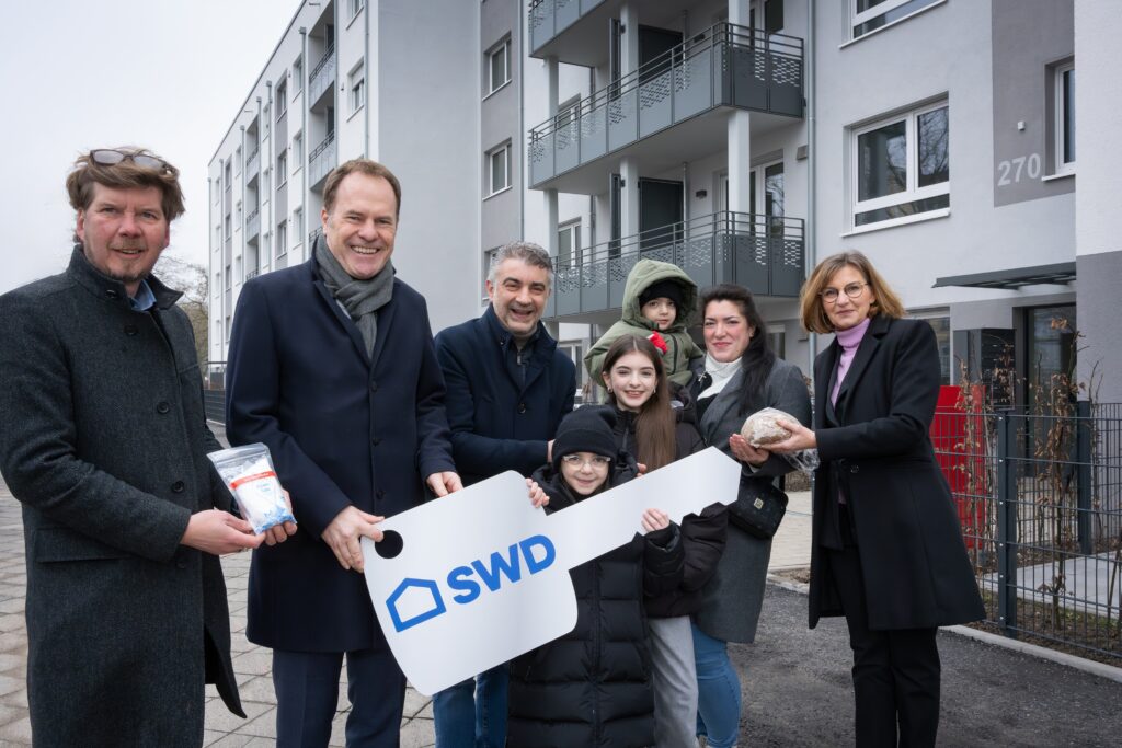 Familie Pignatelli erhält den symbolischen Schlüssel für ihr neues Zuhause aus den Händen des Oberbürgermeisters: von links nach rechts: Klaus Feldhaus (Geschäftsführer SWD), Dr. Stephan Keller (Oberbürgermeister der Landeshauptstadt Düsseldorf),  Familie Pignatelli: Vater Donato, Arianna, Gabriella und Giuseppe auf dem Arm seiner Mutter Mareille, Dr. Eva-Maria Illigen-Günther (Geschäftsführerin SWD © SWD, Fotograf B. Schaller