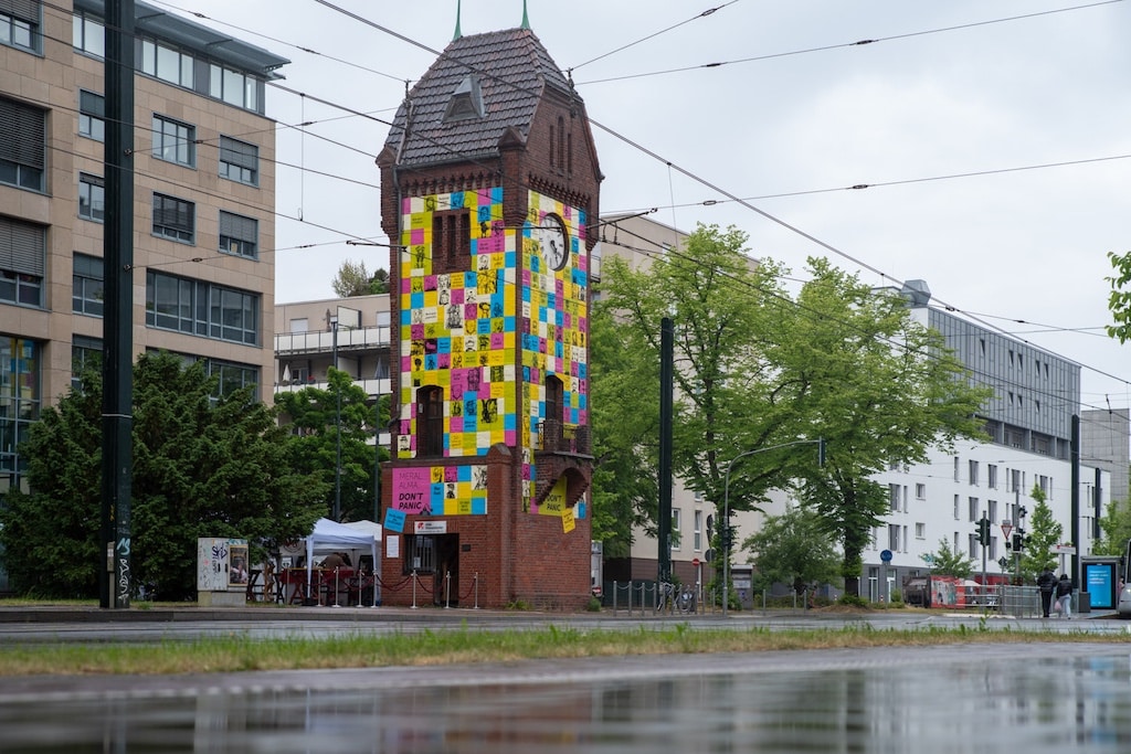 Der historische Uhrenturm an der Grafenberger Allee – vollständig beklebt mit übergroßen Notizzetteln aus Meral Almas Werk „Don’t Panic“ – wird zur begehbaren Projektionsfläche für flüchtige Gedanken, Gesichter und Emotionen. © LB / Olaf oidtmann