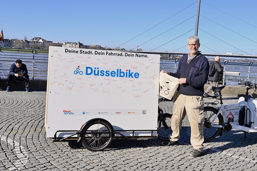 Das Foto zeigt die Situation am Mittwoch auf dem Burgplatz: Dirk Schmit neben dem Anhänger mit der bereits dicht beschriebenen Namenswand – ein sichtbares Zeichen für das große Interesse an der persönlichen Mitgestaltung des neuen Leihsystems. © Lokalbüro