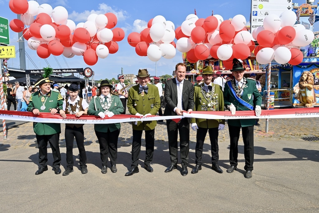 Bandschnitt zur Eröffnung: Oberbürgermeister Dr. Stephan Keller (Mitte) eröffnete die Rheinkirmes 2026 gemeinsam mit Schützenchef Andreas-Paul Stieber, Oberst Torsten Peters, Regimentskönig Jens Linka sowie Vertretern des Regiments und Pagen am Eingang Nord an der Oberkasseler Brücke. © Lokalbüro