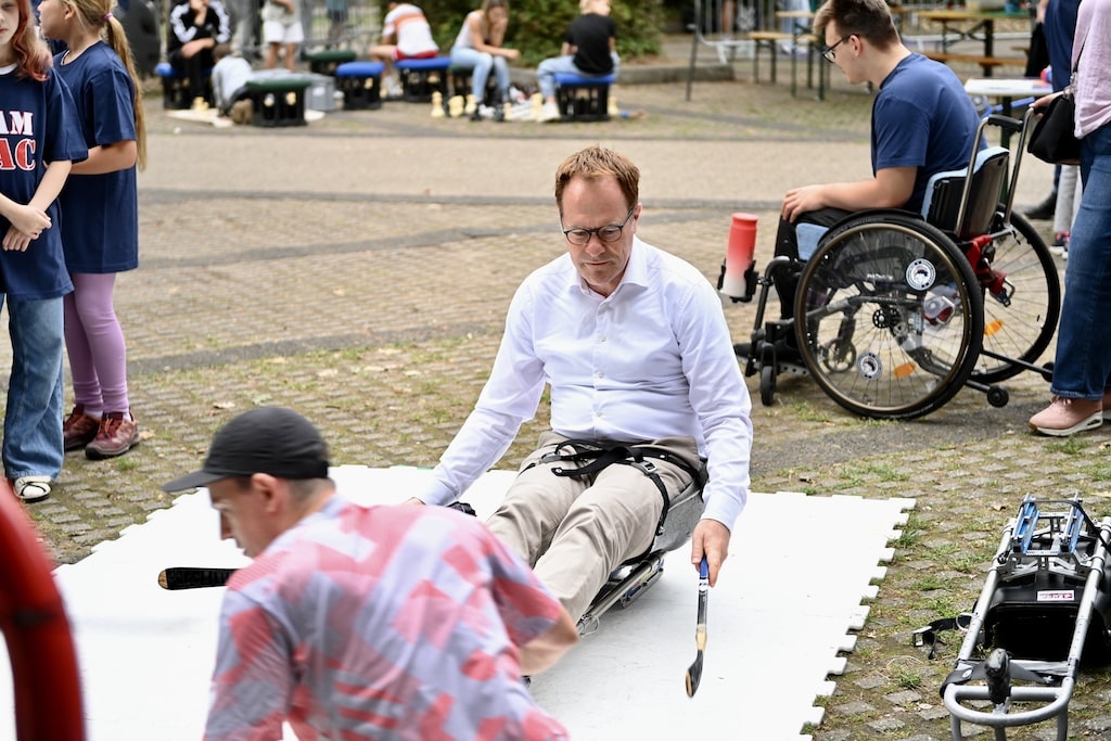 Oberbürgermeister Dr. Stephan Keller nahm beim Para Eishockey der Para-Eishockeytrainingsgruppe Düsseldorf selbst im speziellen Schlitten Platz und stellte sich der Herausforderung gemeinsam mit den Teilnehmenden. Unter Anleitung von Marcel Malchin, der bei den Paralympischen Winterspielen 2026 für die deutsche Mannschaft spielte, wurde schnell klar, wie viel Geschick und Koordination es braucht, sich damit zu bewegen. © Lokalbüro Oberbürgermeister Dr. Stephan Keller nahm beim Para Eishockey der Para-Eishockeytrainingsgruppe Düsseldorf selbst im speziellen Schlitten Platz und stellte sich der Herausforderung gemeinsam mit den Teilnehmenden. Unter Anleitung von Marcel Malchin, der bei den Paralympischen Winterspielen 2026 für die deutsche Mannschaft spielte, wurde schnell klar, wie viel Geschick und Koordination es braucht, sich damit zu bewegen. © Lokalbüro
