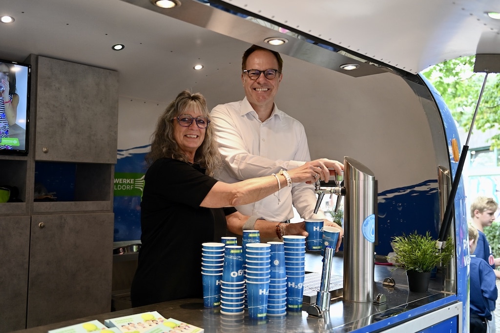 Auch am Wasserwagen der Stadtwerke Düsseldorf ließ es sich Oberbürgermeister Dr. Stephan Keller nicht nehmen, selbst mit anzupacken: Gemeinsam mit einer Mitarbeiterin der Stadtwerke zapfte er einige Becher frisches Trinkwasser und verteilte sie an die Besucherinnen und Besucher des Olympic Adventure Camps. © Lokalbüro